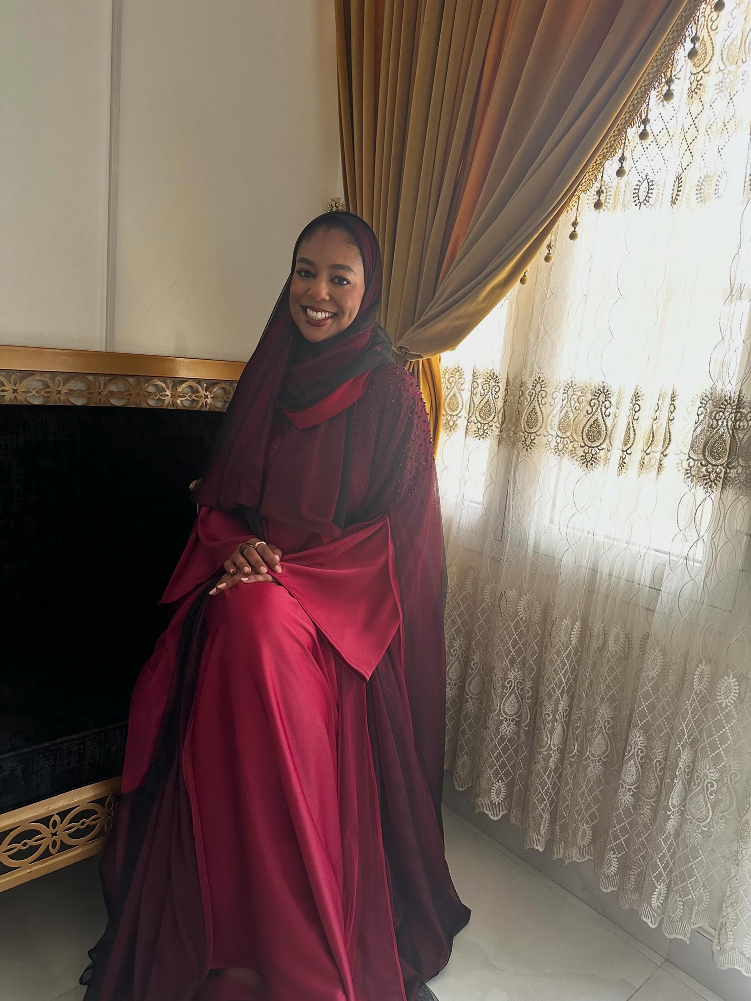 Asma Al Riyami in a burgundy abaya by a window